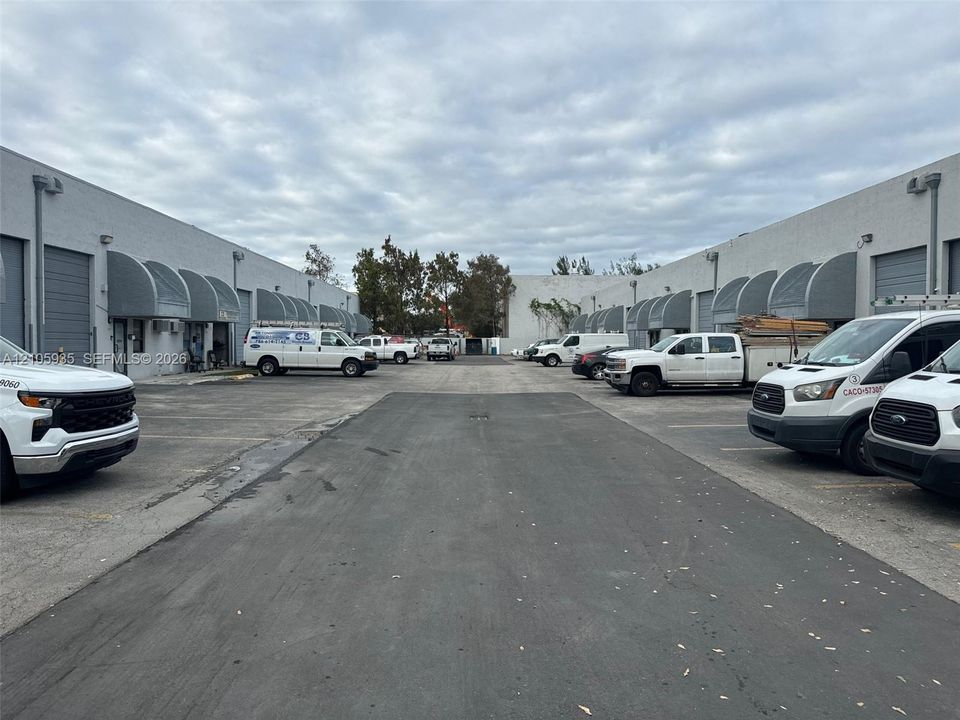 Commercial property exterior featuring a central paved driveway, concrete block construction, and individual metal roll-up doors with metal awnings