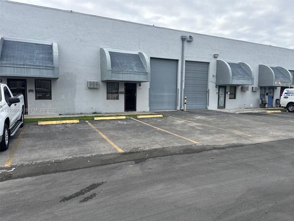 Commercial facility featuring concrete exterior, two roll-up doors, multiple entry points, and dedicated asphalt parking