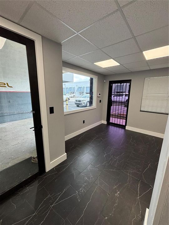 Dark tile flooring with veining, drop ceiling with recessed panel lighting, large picture window, and metal-framed security door