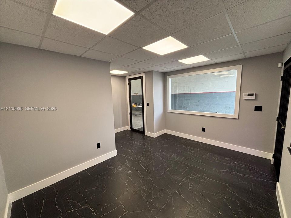 Interior space featuring dark stone-finish tile flooring, recessed drop ceiling with integrated lighting, glass-paneled entry door, and an interior fixed-pane window