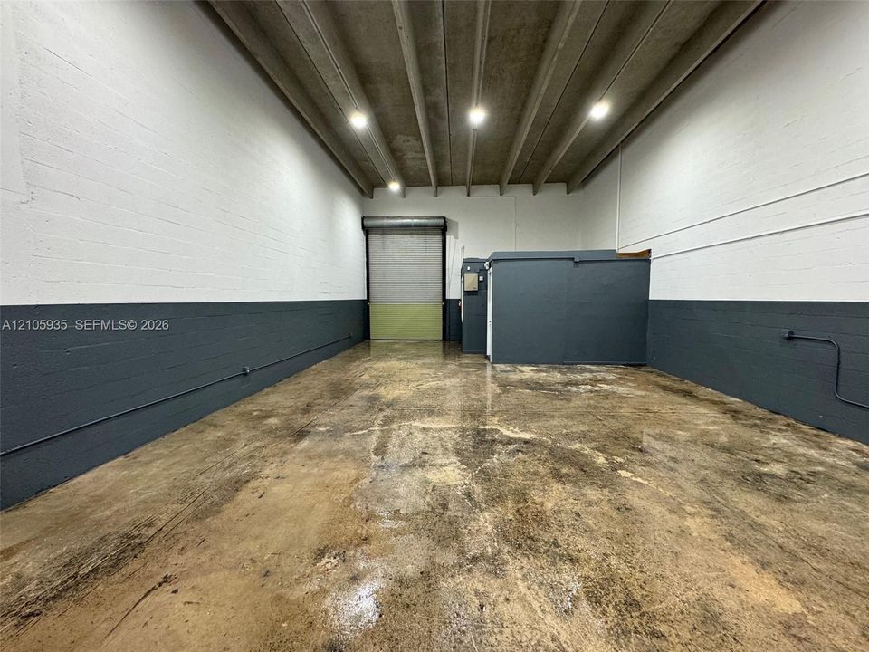 Industrial space featuring high-clearance exposed beam ceilings, finished concrete flooring, painted masonry walls, and a large metal roll-up door
