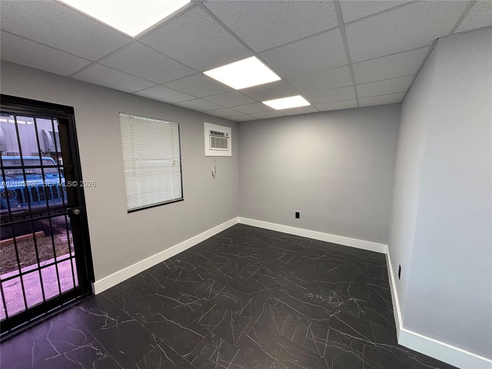 Interior space featuring dark stone-finish tile flooring, inset ceiling lighting, a singular window with horizontal blinds, and a metal security door