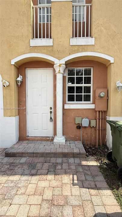 Stucco exterior featuring dual arched entryways, a central decorative column, grid-patterned windows, and paver-stone entry flooring