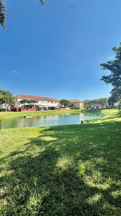 Waterfront setting featuring a central pond, expansive lawn, mature palm trees, and terracotta-tiled roof architecture