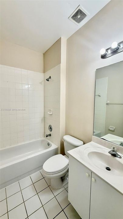 Bathroom featuring a white vanity cabinet with an integrated sink, wall-mounted mirror, ceramic tile flooring, and a shower-tub combination with white tile surround
