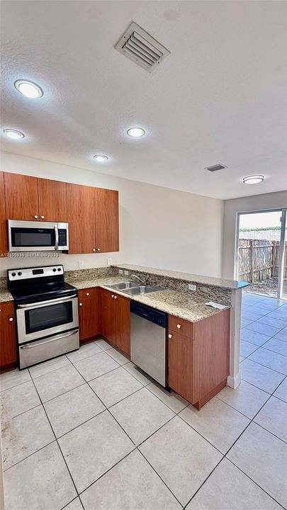 Kitchen featuring wood cabinetry, stone countertops, stainless steel appliances, and ceramic tile flooring
