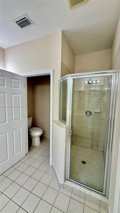 Corner glass-enclosed shower with tiled surround, porcelain tile flooring, and separate water closet