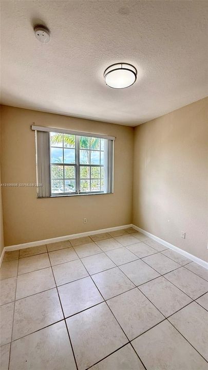 Room featuring neutral wall tones, large-format tile flooring, a multi-pane window with vertical blinds, and a round flush-mount ceiling fixture