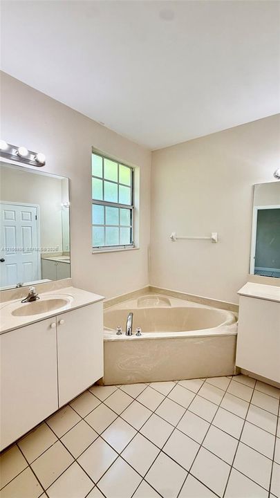 Dual vanity with integrated sinks, corner soaking tub, ceramic tile flooring, and wall-mounted vanity lighting