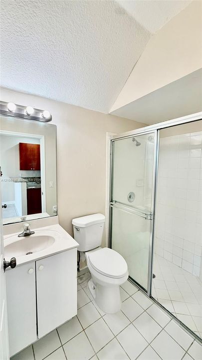 Bathroom featuring a single-sink vanity with white cabinetry, a glass-enclosed shower with tiled walls, ceramic floor tiling, and wall-mounted light fixtures above the mirror