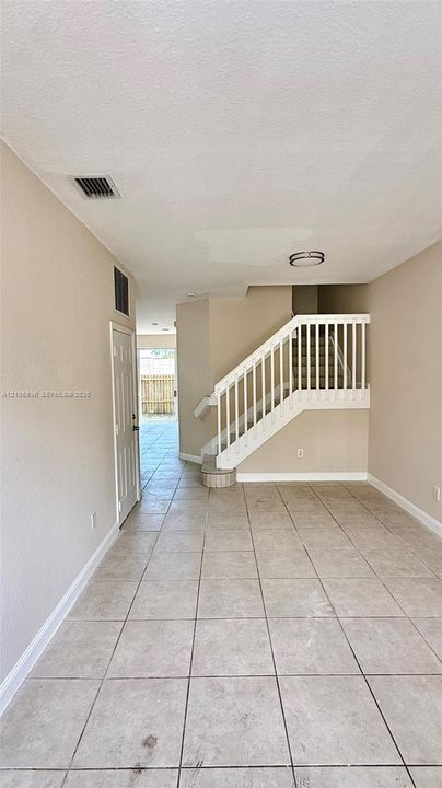 Interior space featuring neutral wall tones, large-format tile flooring, a white-railed staircase, and a flush-mount ceiling light fixture