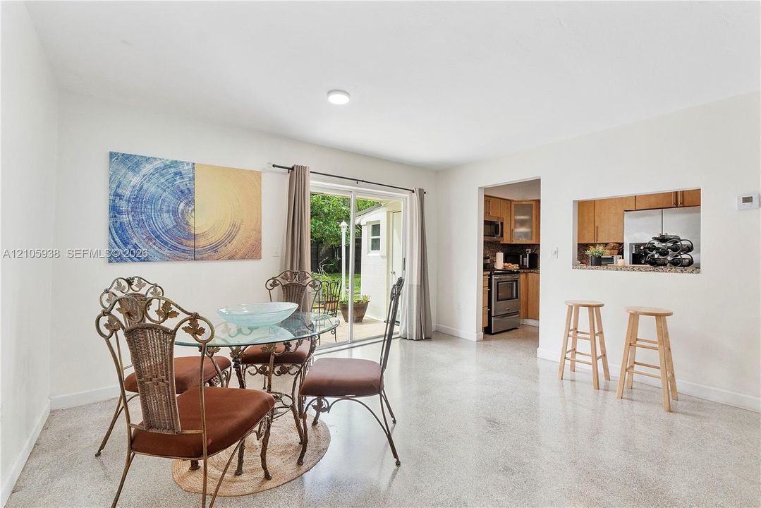 Neutral-toned interior space featuring polished concrete flooring, a sliding glass door providing exterior access, and a kitchen pass-through window with a countertop ledge