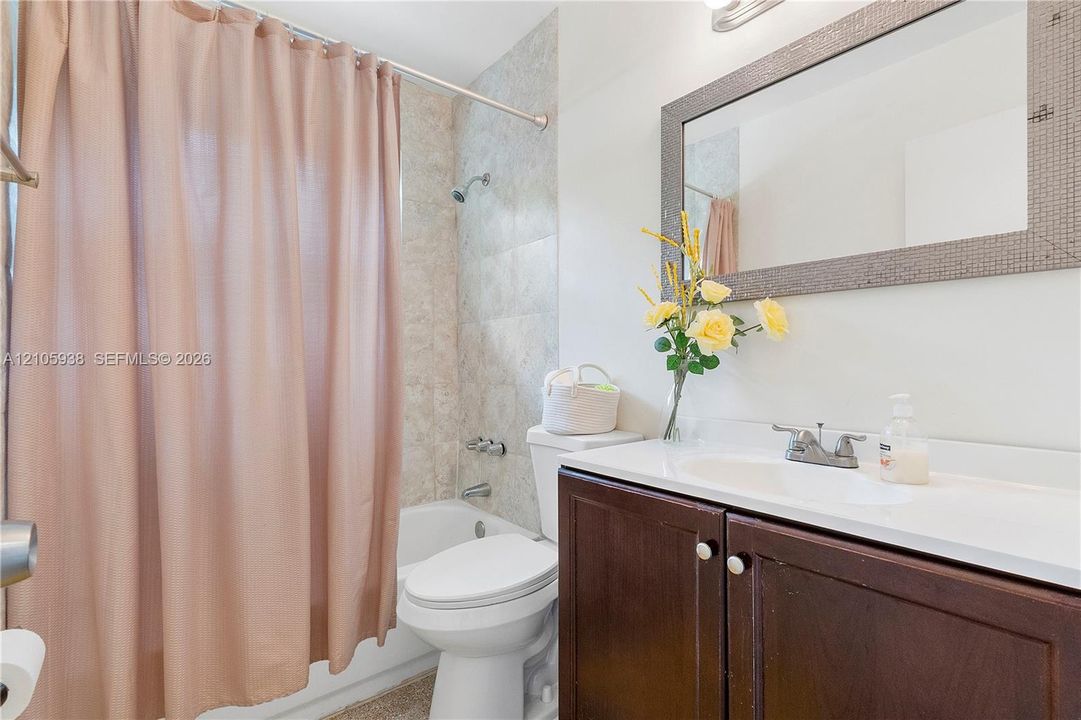 Bathroom featuring a vanity with dark-finish cabinetry, a white integrated countertop and basin, a framed wall mirror, and a tub-shower combination with neutral-toned wall tile