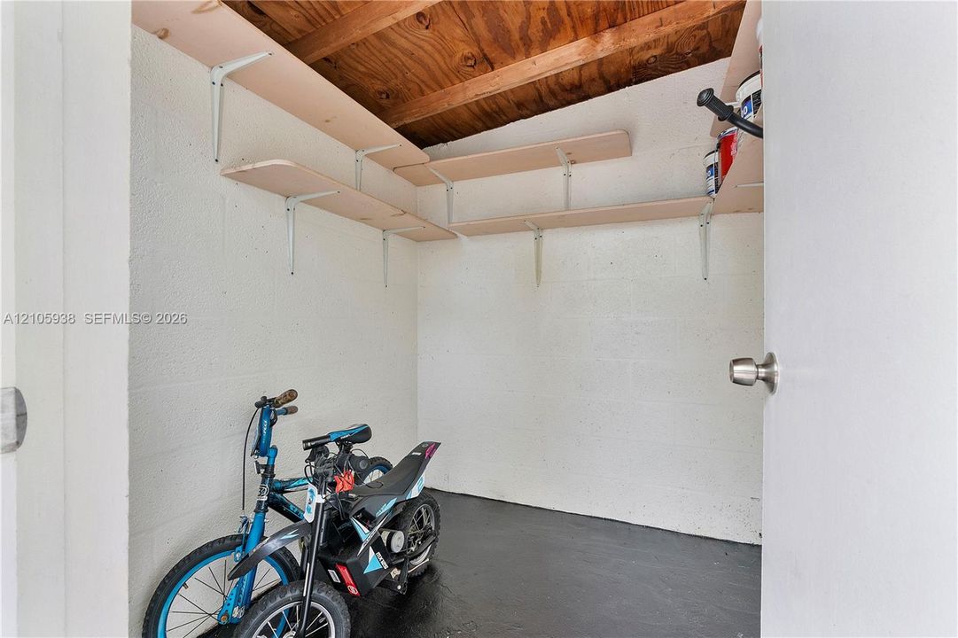 Storage area featuring painted concrete block walls, exposed wood ceiling rafters, and tiered wood shelving units