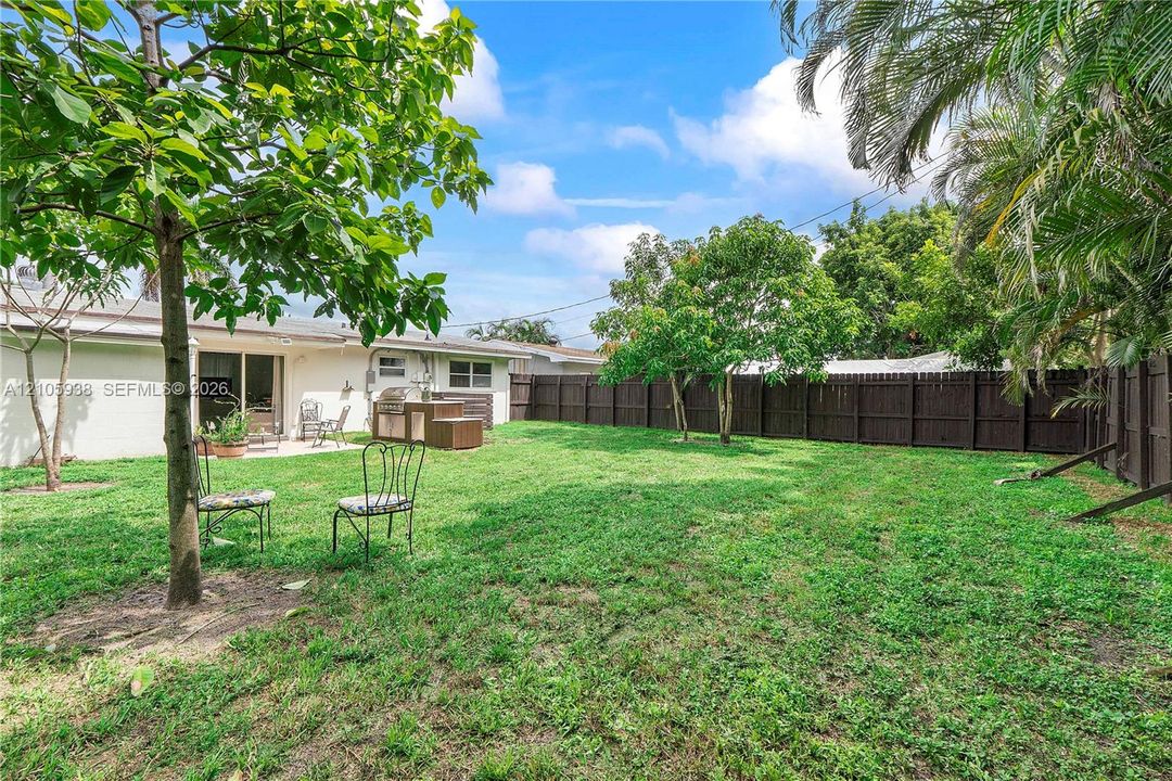 Backyard featuring a grass lawn, mature trees, wood privacy fencing, and a concrete patio