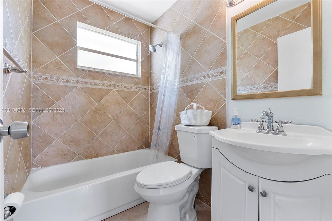 Bathroom featuring diamond-patterned wall tiling with decorative border inlay, porcelain tub-shower combination, and white vanity cabinet with a curved basin and chrome fixture
