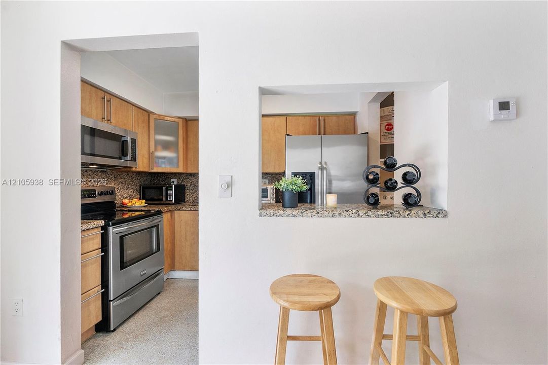 Kitchen featuring wood cabinetry, stone-finish countertops, stainless steel appliances, and a pass-through opening with a breakfast bar