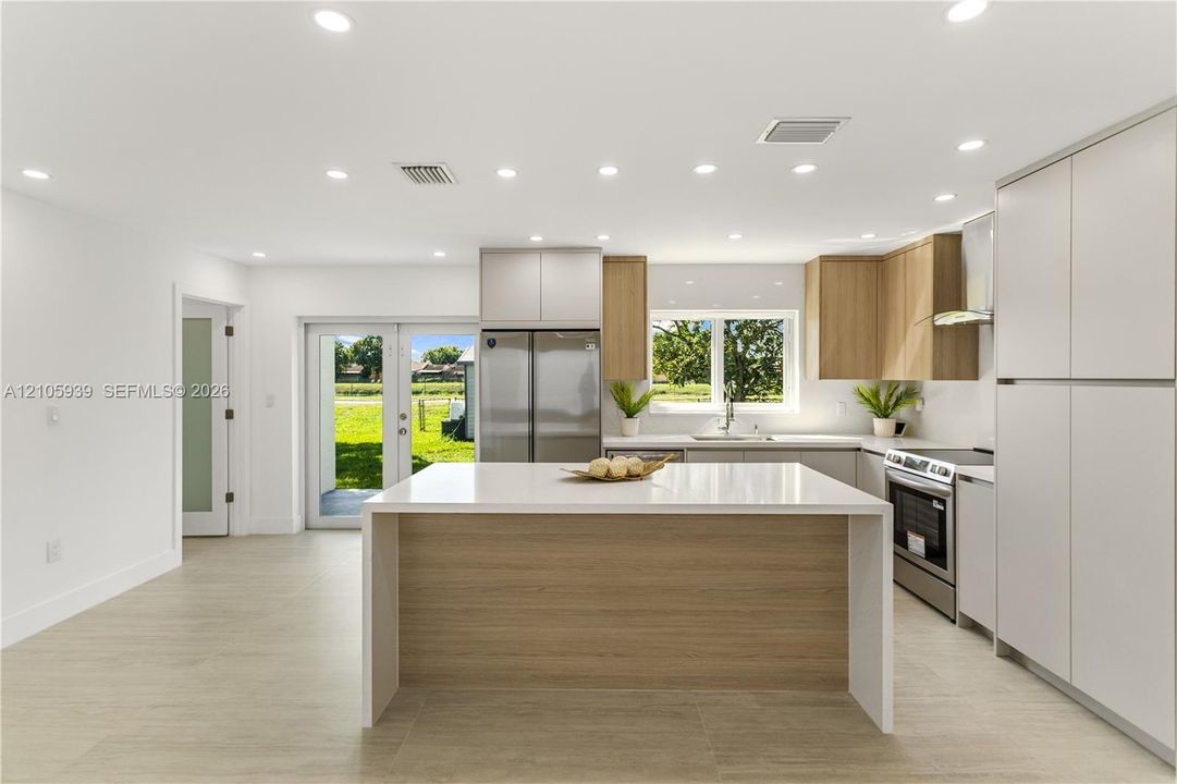 Kitchen featuring two-tone cabinetry, a central island with white stone-finish countertop, stainless steel appliances, recessed ceiling lighting, and wood-finish flooring