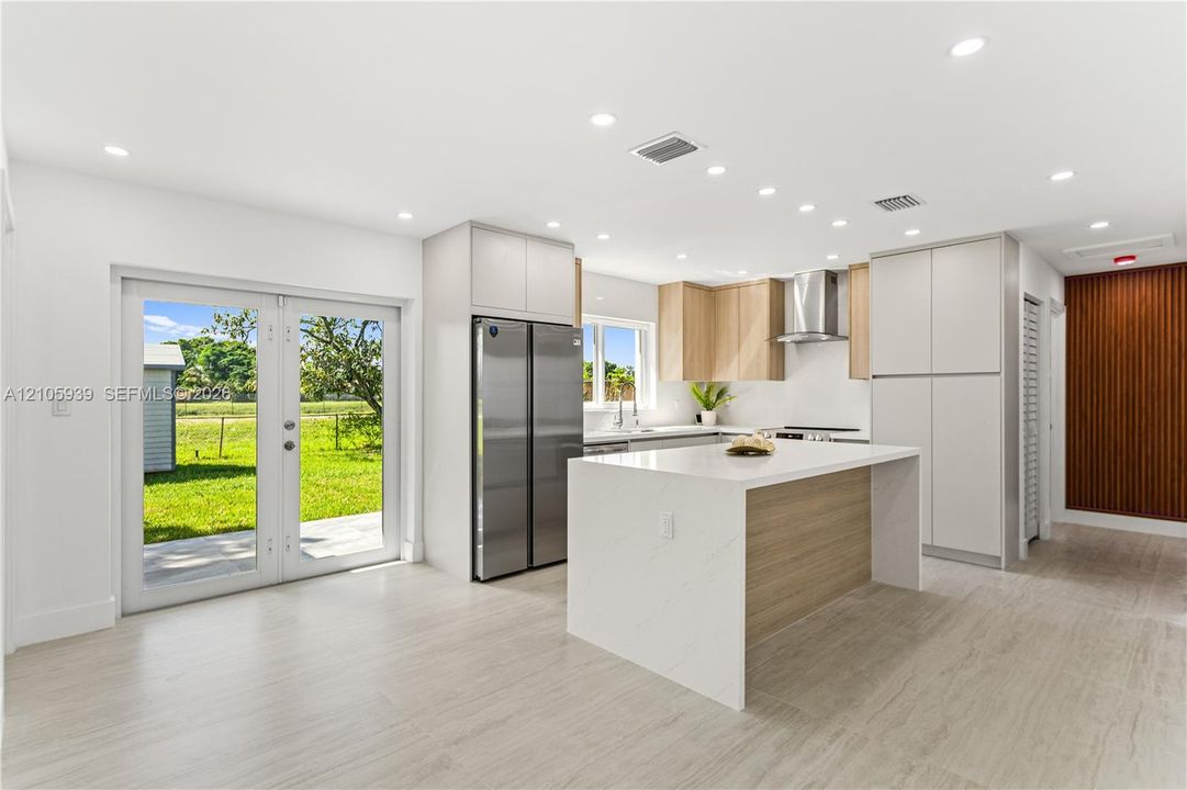 Kitchen featuring a central island with a solid surface countertop, stainless steel refrigerator, recessed lighting, double glass doors, and tile flooring