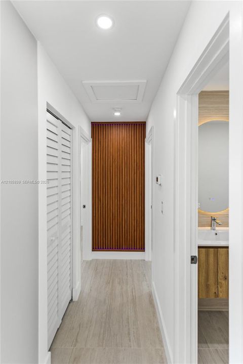 Hallway featuring wood-slat accent wall, white louvered closet doors, recessed lighting, and wood-finish flooring