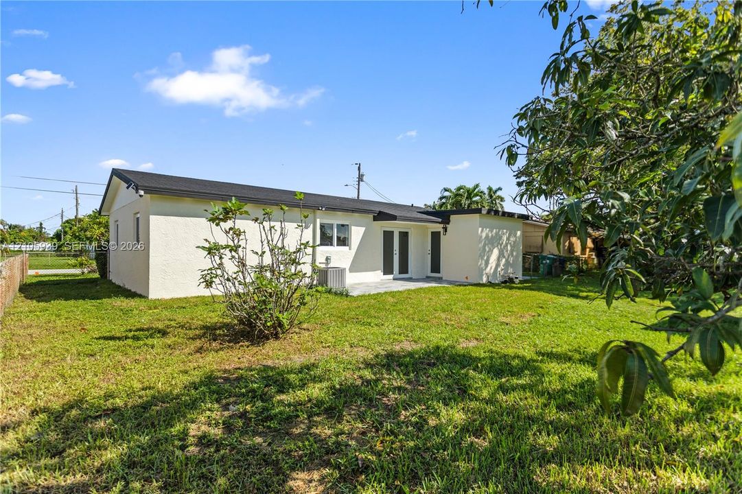 Rear exterior featuring a smooth stucco facade, dark shingled roof, glass sliding doors, and a sprawling grass yard