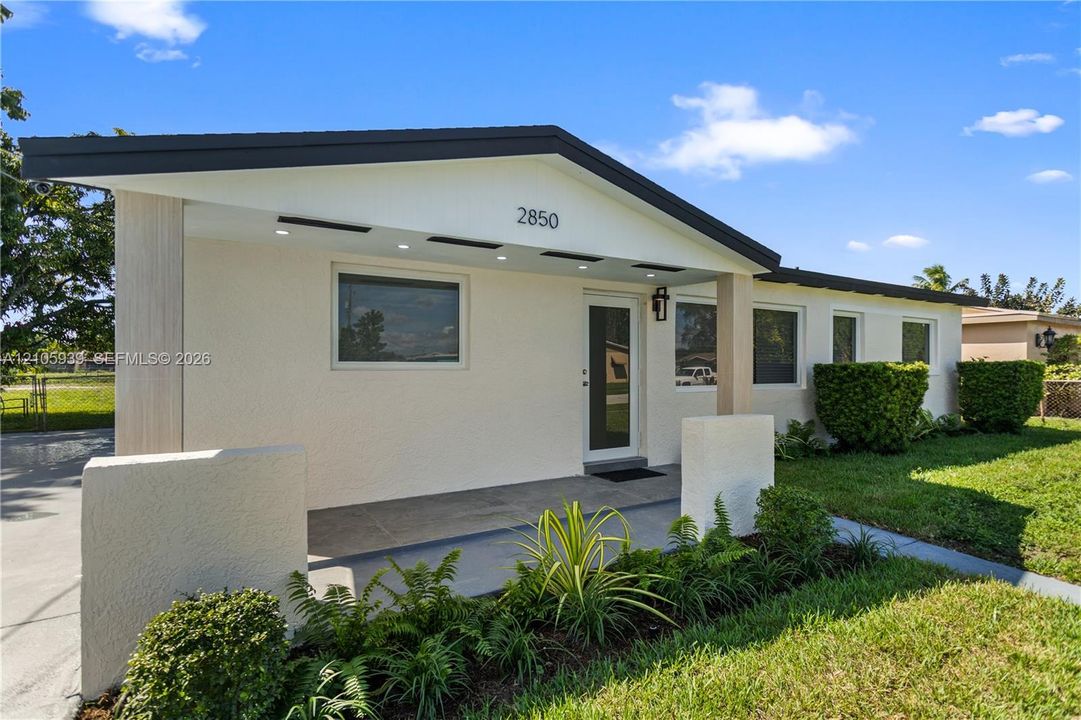 Single-story exterior featuring a textured stucco facade, covered porch with recessed lighting, and architectural gable roofline