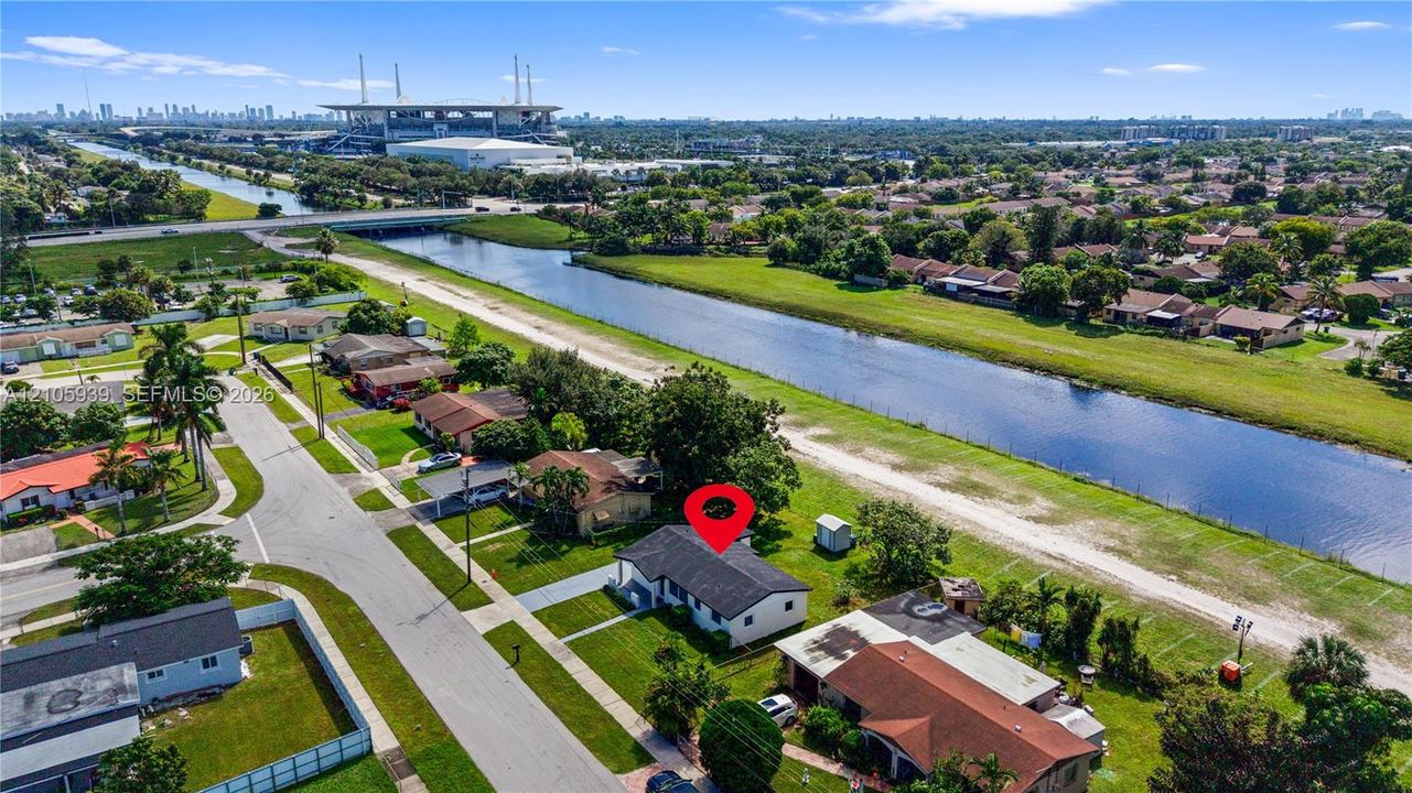 Aerial perspective of a detached single-story residence situated along a canal-front lot, featuring a shingled roof, concrete driveway, and established lawn