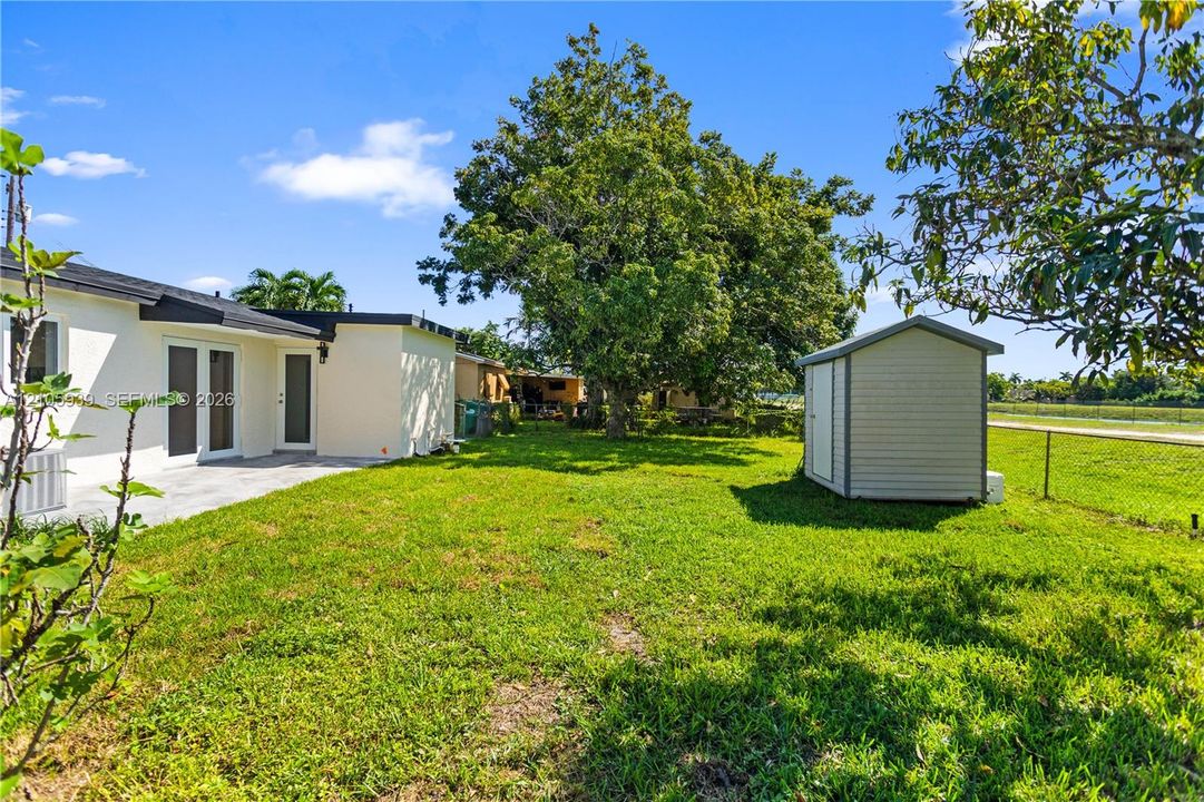 Backyard featuring a concrete patio, freestanding storage shed, established trees, and chain-link fencing