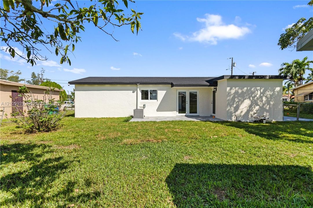 Exterior elevation featuring a light-colored stucco finish, dark-toned roofline, glass-paneled double doors, and an expansive rear lawn