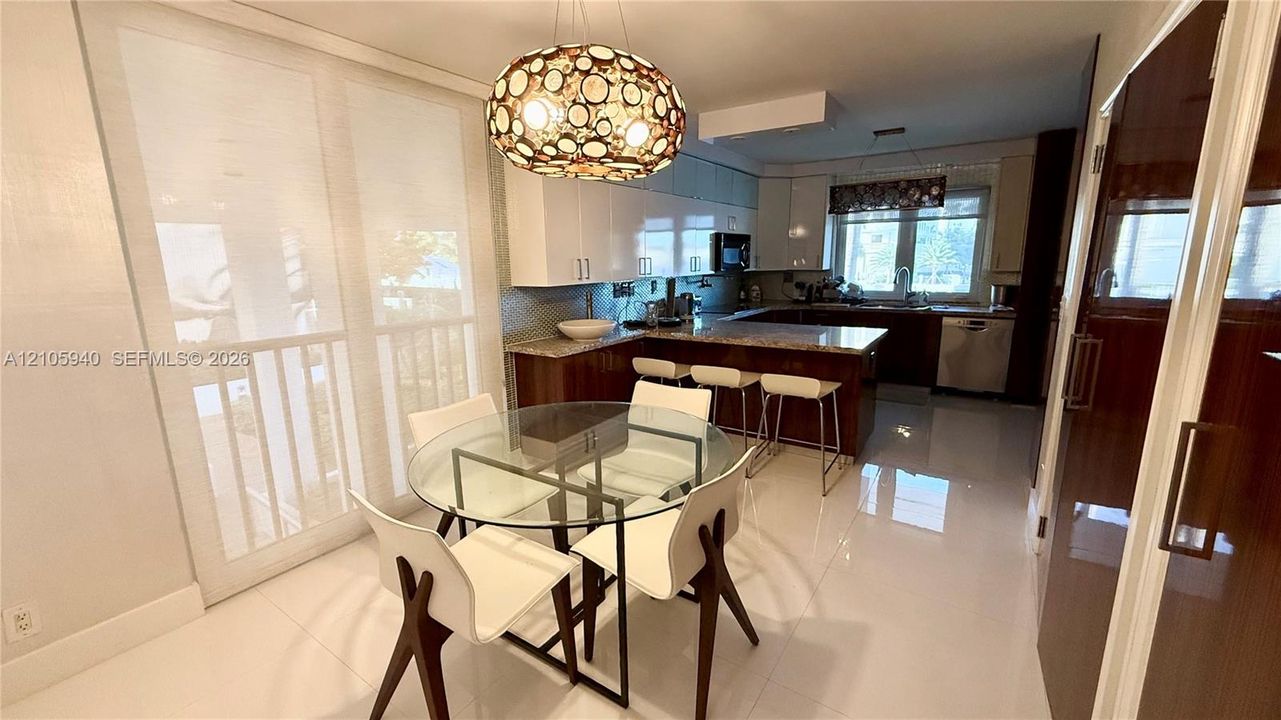 Kitchen area featuring high-gloss cabinetry, stone countertops, a multi-level breakfast bar, large-format tile flooring, and a decorative orb-style pendant light fixture