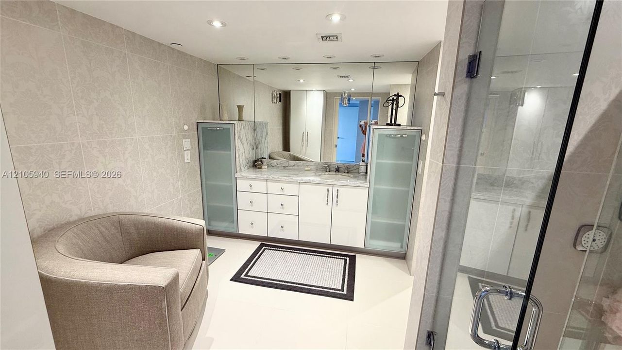 Built-in vanity featuring high-gloss cabinetry, stone countertops, integrated side storage towers with glass-panel doors, and a full-width wall mirror