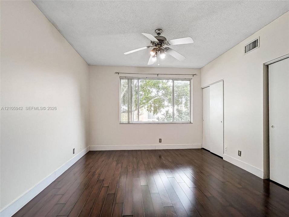 Room featuring wood-finish flooring, a ceiling fan with integrated light fixture, and a sliding-door closet
