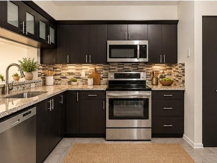 Staged-Kitchen featuring dark wood cabinetry, stainless steel appliances, multi-tonal tile backsplash, stone-finish countertops, and an undermount sink