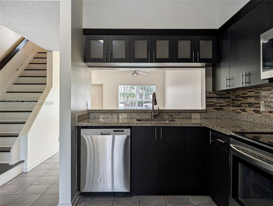 Kitchen featuring dark-finish flat-panel cabinetry, stone-style countertops, stainless steel dishwasher, and horizontal mosaic tile backsplash
