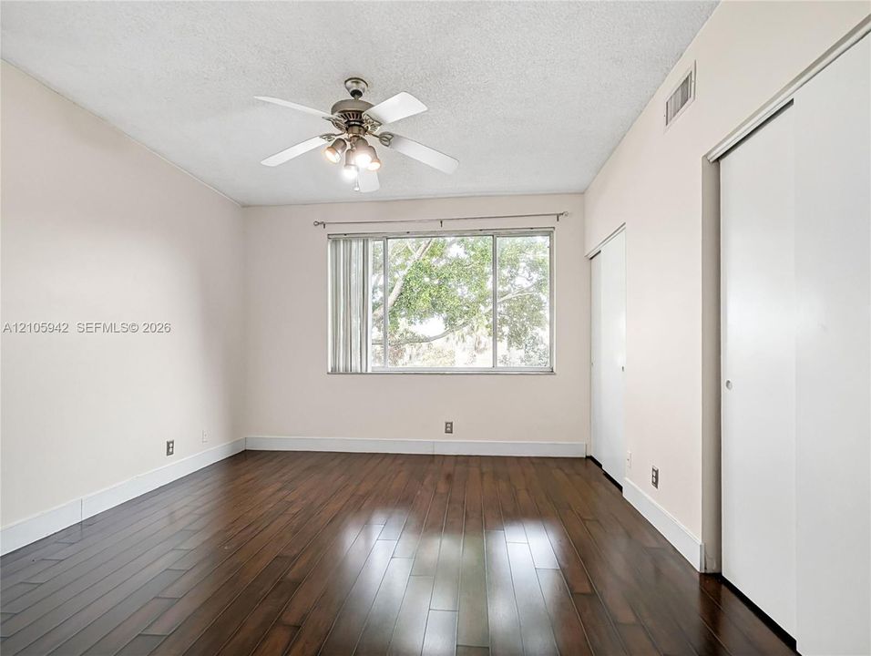 Room featuring wood-finish flooring, a ceiling fan with integrated lighting, and built-in sliding door closet storage