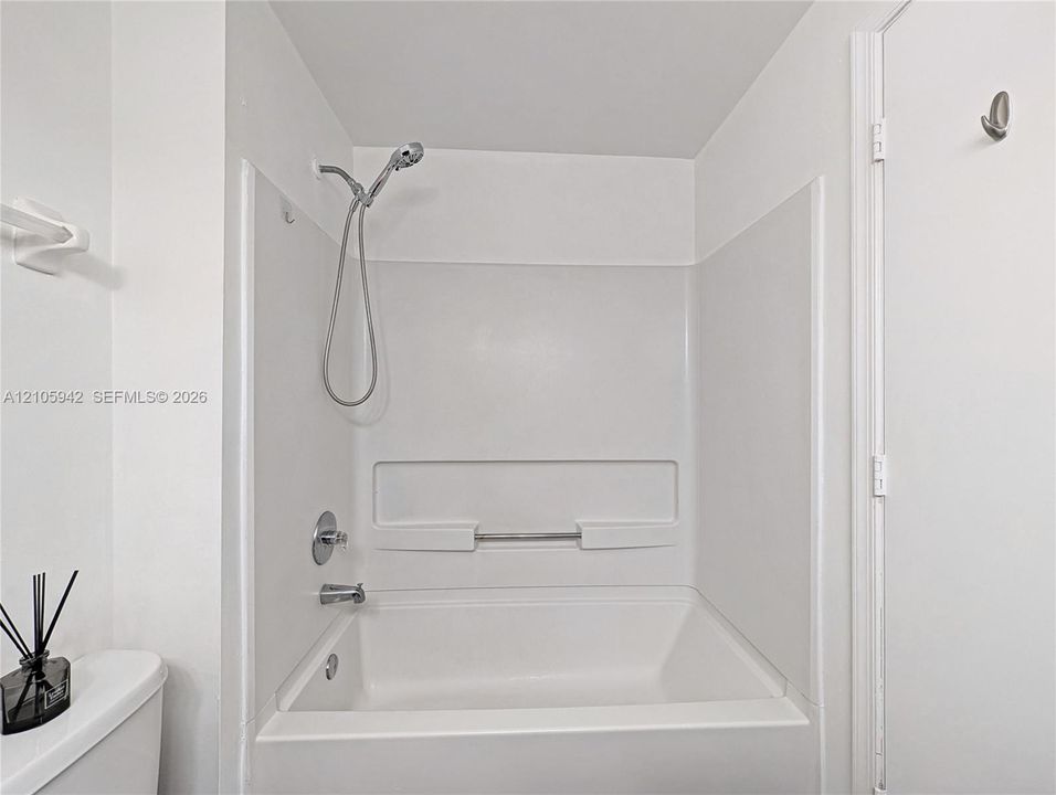 Tub-shower combination featuring a white surround, integrated shelving, and a chrome handheld shower head