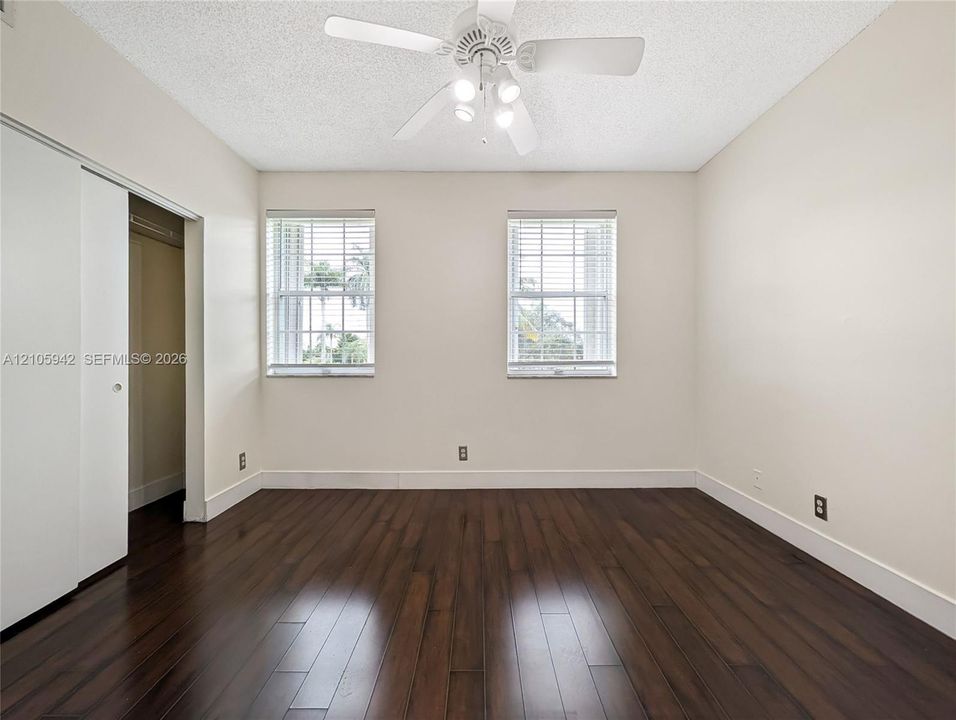 Wood-finish flooring, dual windows with horizontal blinds, white sliding closet doors, and ceiling fan with integrated lighting