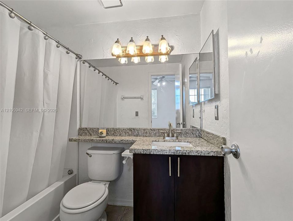 Bathroom featuring a vanity with stone-finish countertop, undermount sink, multi-light fixture, and large wall-mounted mirror