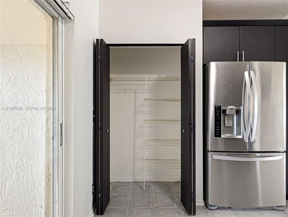 Stainless steel french-door refrigerator with built-in water dispenser, dark-toned cabinetry, and walk-in storage closet with wire shelving