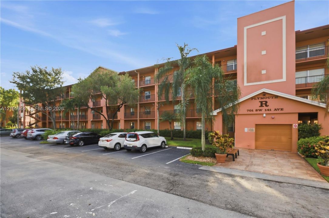 Multi-story residential building exterior featuring stucco cladding, balconies with metal railings, and ground-level garage access