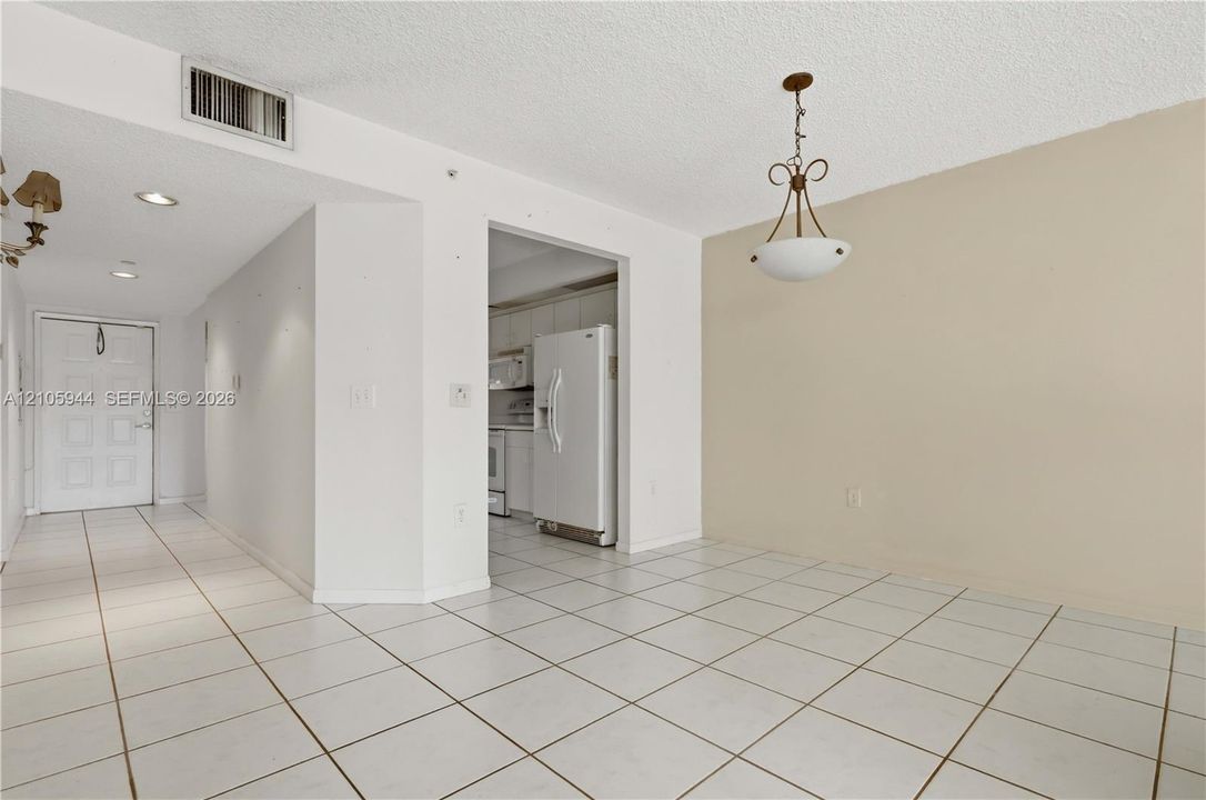 Open-concept interior featuring light-toned tile flooring, a multi-light pendant fixture, recessed ceiling lighting, and a six-panel entry door