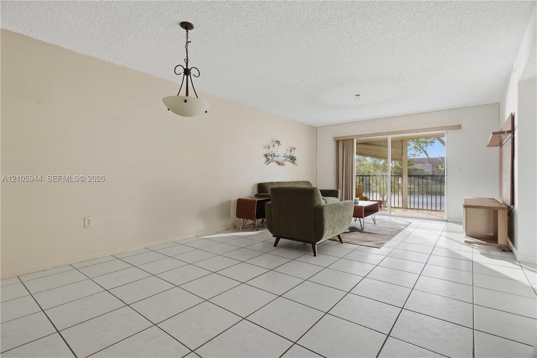 Open living area featuring large-format ceramic floor tiling, a multi-light pendant fixture, and sliding glass doors with direct access to a private balcony