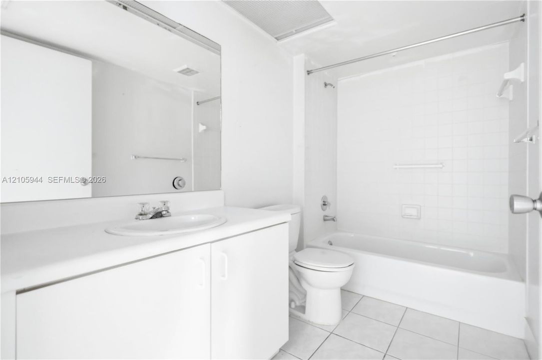 Bathroom featuring a single-sink vanity with a solid-surface countertop, an expansive wall-mounted mirror, a tiled shower-tub combination, and ceramic tile flooring
