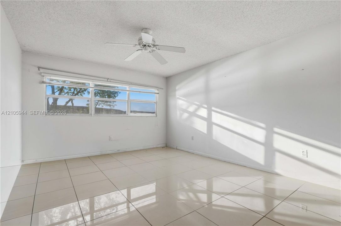 Neutral-toned interior featuring large-format polished tile flooring, white walls, and a ceiling-mounted fan with integrated lighting