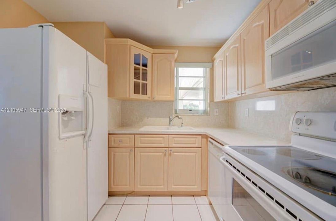 Kitchen featuring light-finish wood cabinetry, a double-basin sink with a chrome faucet, tile flooring, and a glass-front upper cabinet