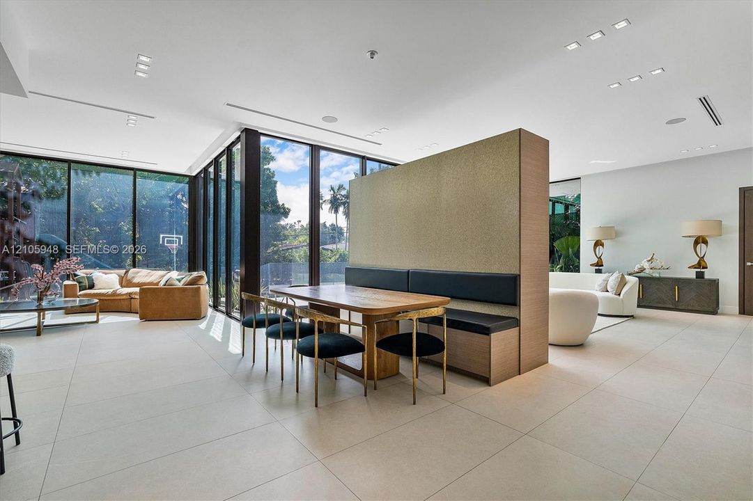 Open-concept interior featuring expansive floor-to-ceiling windows, large-format tile flooring, recessed ceiling lighting, and a custom architectural room divider with integrated bench seating