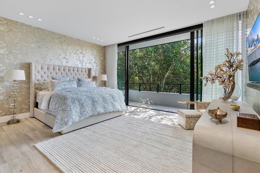 Floor-to-ceiling sliding glass doors opening to a balcony, light-toned wood-finish flooring, recessed ceiling lighting, and patterned wallpaper feature wall