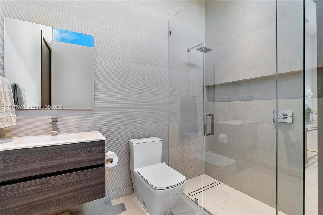Floating vanity with wood-finish cabinetry, rectangular vessel sink, wall-to-wall mirror, glass-enclosed shower with rainfall showerhead, and wall-mounted plumbing fixtures