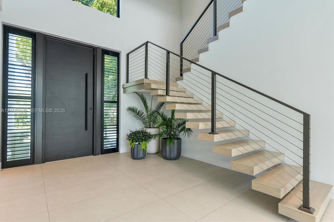 Foyer featuring a large-format tile floor, a solid front door with floor-to-ceiling sidelights, and an open-riser staircase with wood-finish treads and metal cable railing
