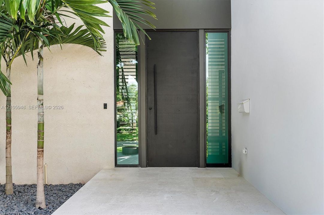 Entry featuring a dark horizontal-plank door with an elongated vertical handle, framed by full-height frosted glass sidelights on a neutral-toned stone landing